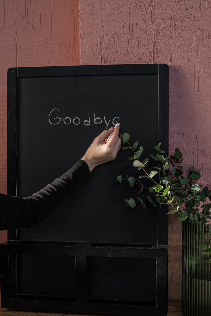 person writing "goodbye" on black board with chalk